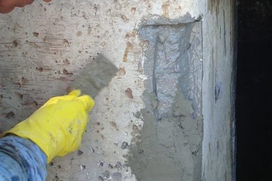 Applicator troweling repair mortar into a patch on a concrete column