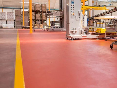 Red resinous floor coating with a yellow safety line in a production plant