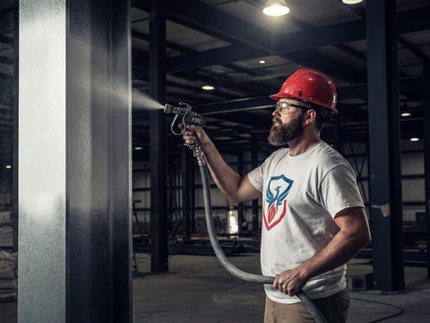 Applicator spraying fireproofing coating on a structural steel column