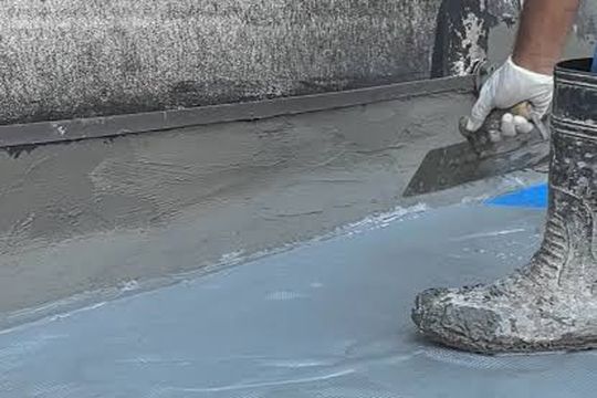Applicator troweling a waterproofing membrane up a wall