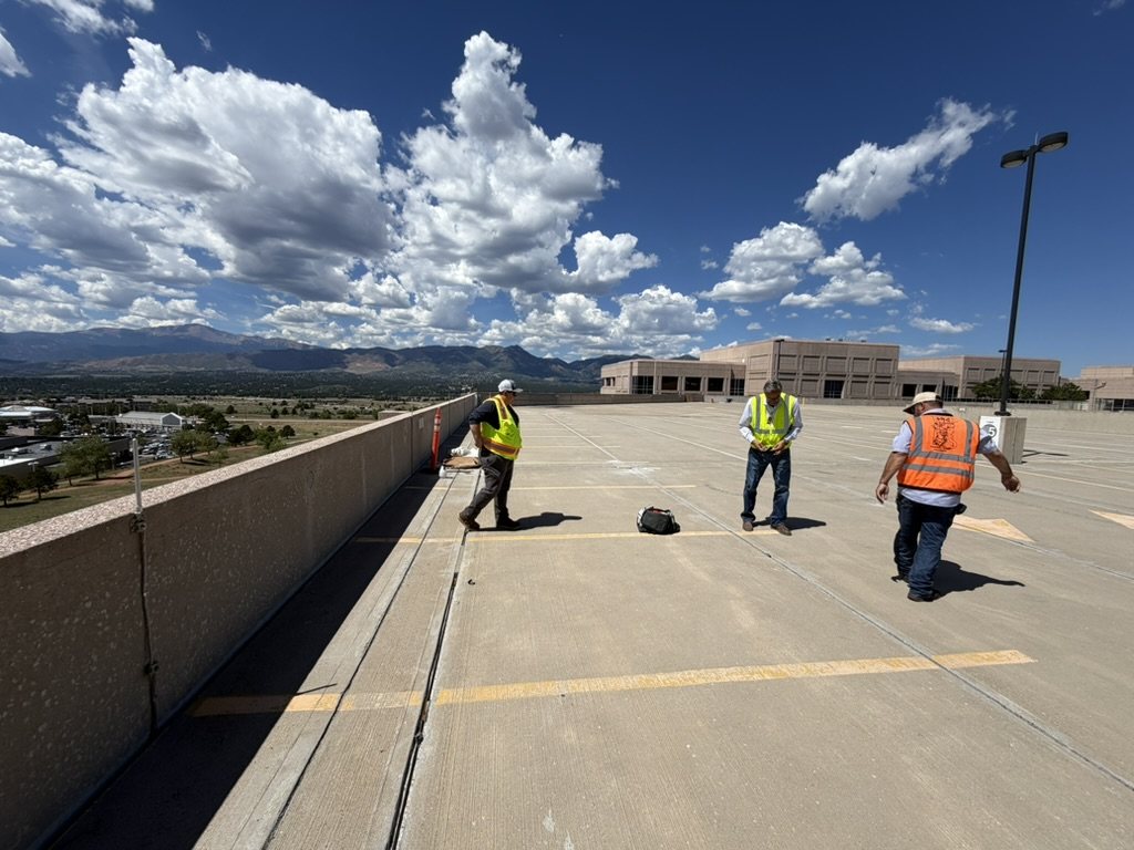 Crew in safety vests evaluating a parking deck with the Colorado Front Range behind them